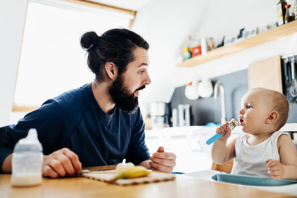 Single father sat at the kitchen table helping his baby eat