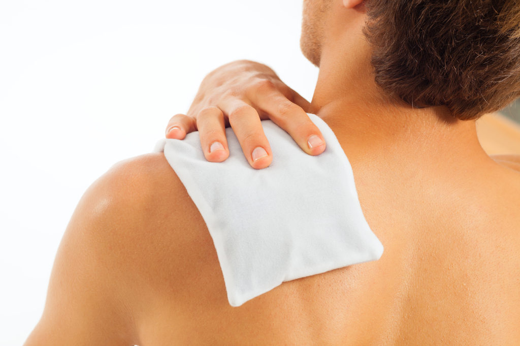 Man places heating pad or cool pack on shoulder