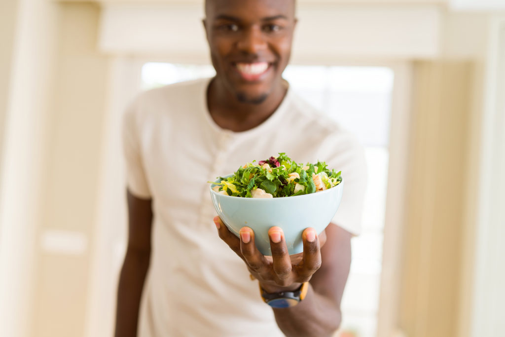 African young man holding a bowl of healthy salad