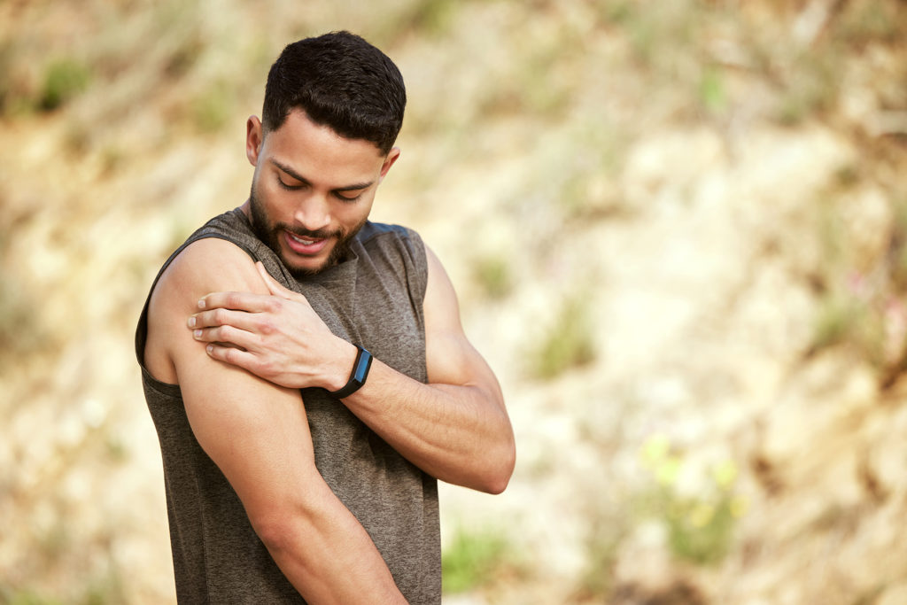 Shot of a sporty young man holding his shoulder in pain while exercising outdoors