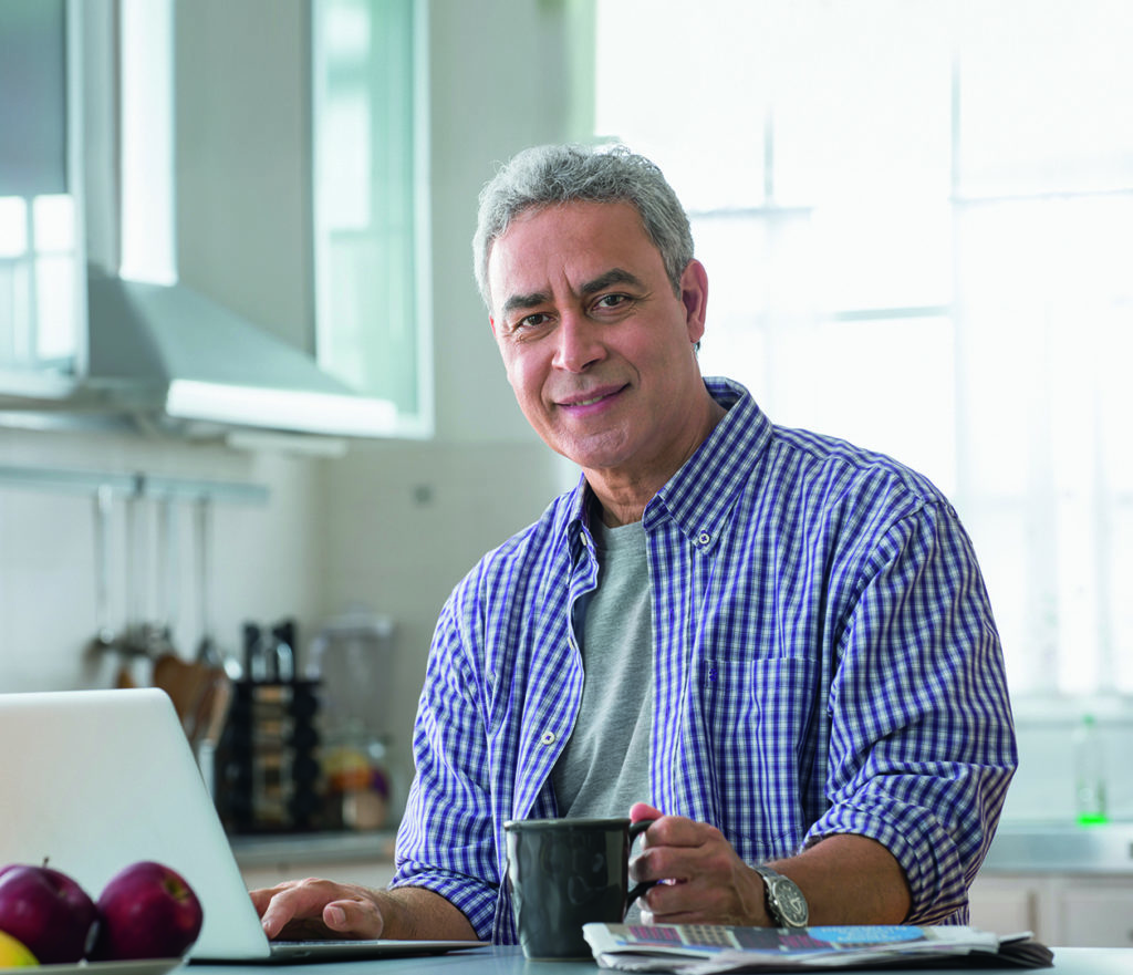 Hispanic man using laptop at kitchen table