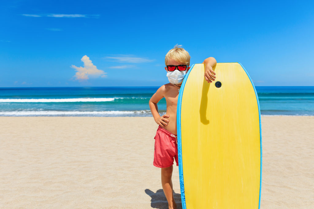 Young surfer wearing sunglasses, protective mask on sea beach