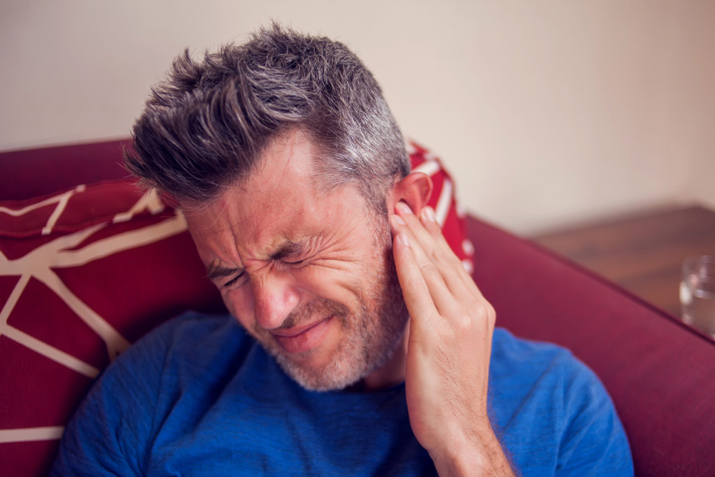 Man feels ear because of tinnitus.