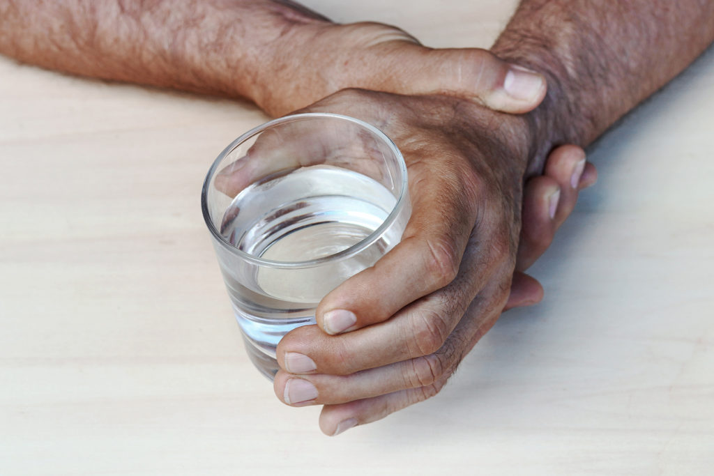 hands of a man with Parkinson's trying to hold a water glass