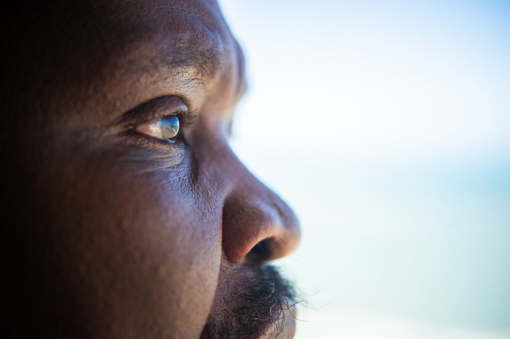 Black senior man looks out window. Close up.