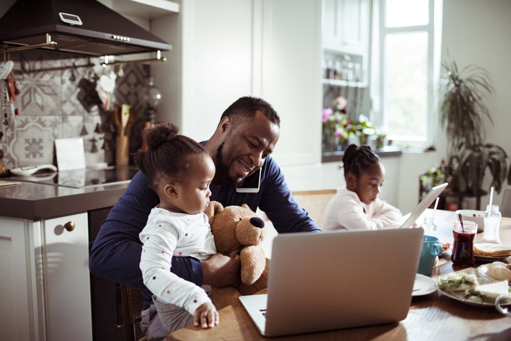 Father with toddlers trying to work at kitchen table