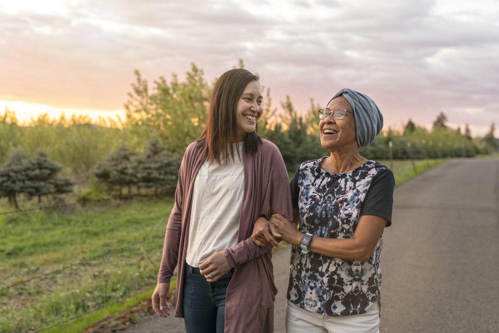 senior woman with cancer walks with her daughter at sunset