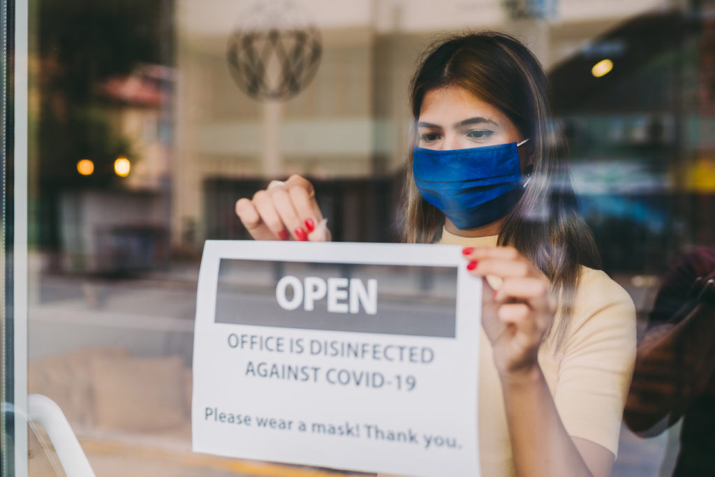 Businesswoman putting open COVID sign on front office