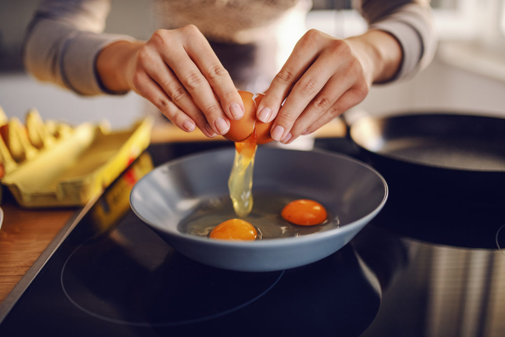Woman breaks egg over pan