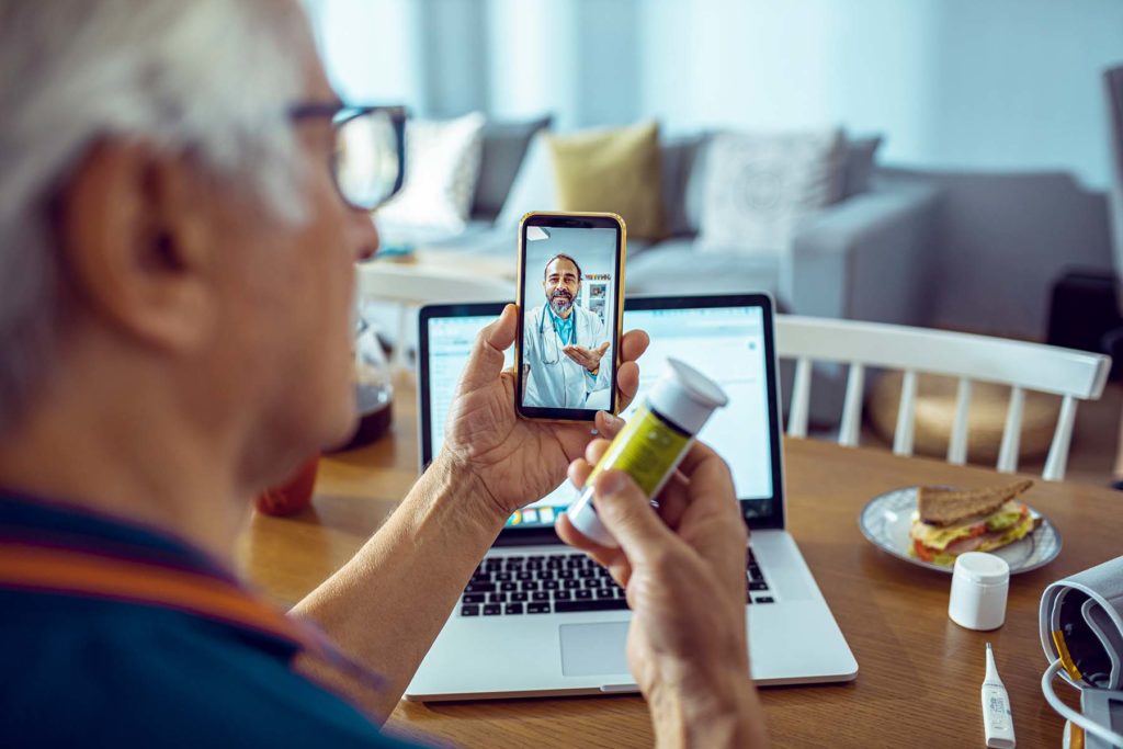 Senior man holds pill bottle during telehealth call